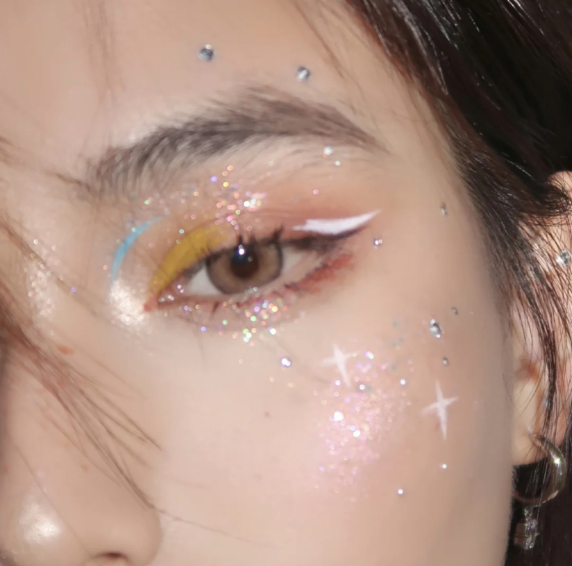 接着就用大颗粒亮片眼影提亮眼窝和卧蚕的部位，再用黑色眼线笔画出上扬的眼线。然后用白色眼线笔叠加画在黑色眼线上，最后可以在腮红的部位画出亮片效果。