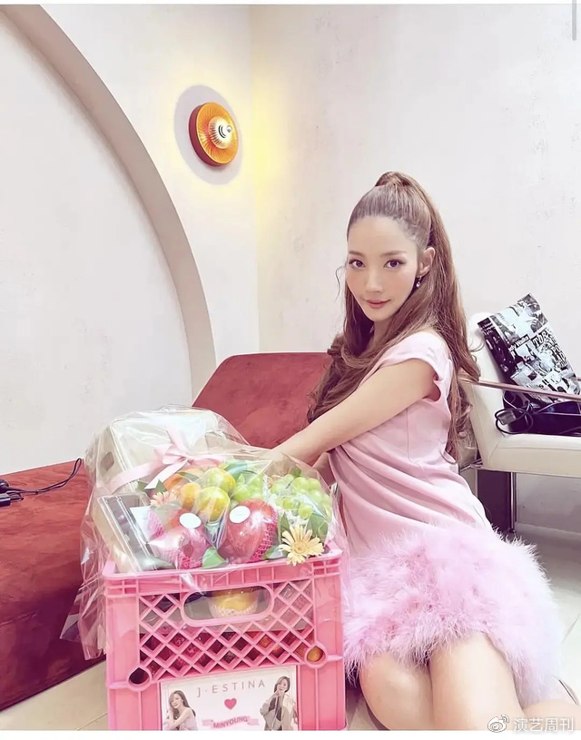 只见照片中的她,身穿粉色的连衣裙,并将头发梳成高马尾坐在沙发上,面带微笑看着镜头。